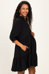 woman wearing a black maternity dress with a tiered skirt and pockets, holding her baby bump and smiling