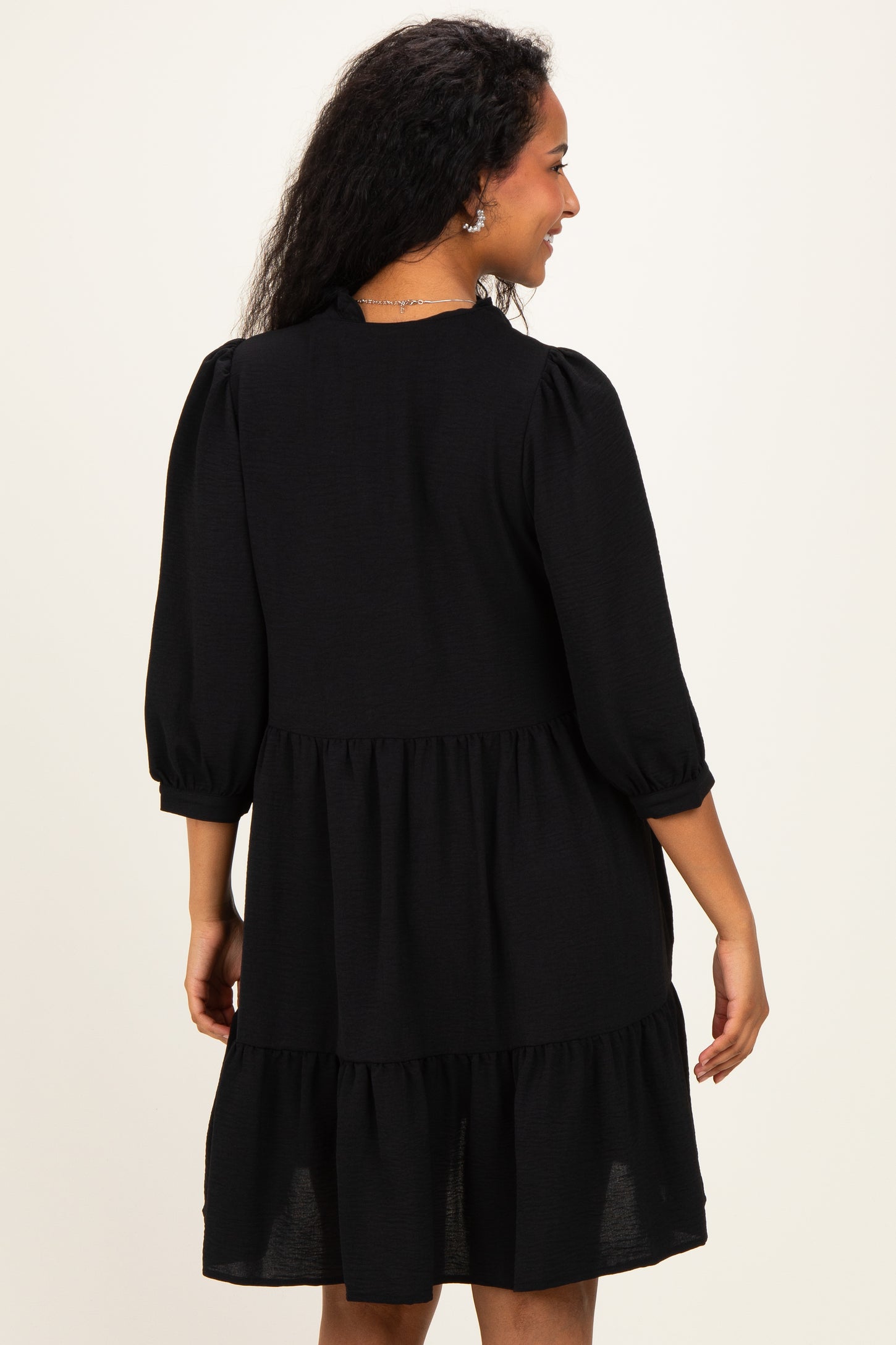 woman wearing a black maternity dress with three-quarter sleeves and a tiered skirt, showing a relaxed fit from the back