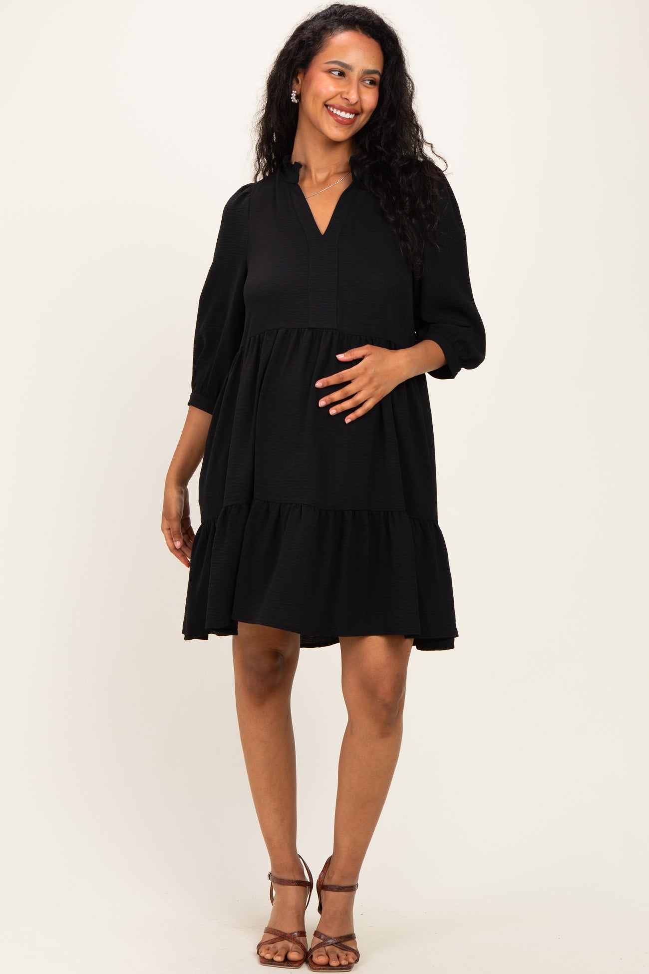 woman wearing a black maternity dress with three-quarter sleeves and a tiered skirt, showing her baby bump