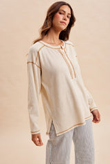 woman wearing a beige long sleeve henley top with button details and contrast stitching, styled with striped pants