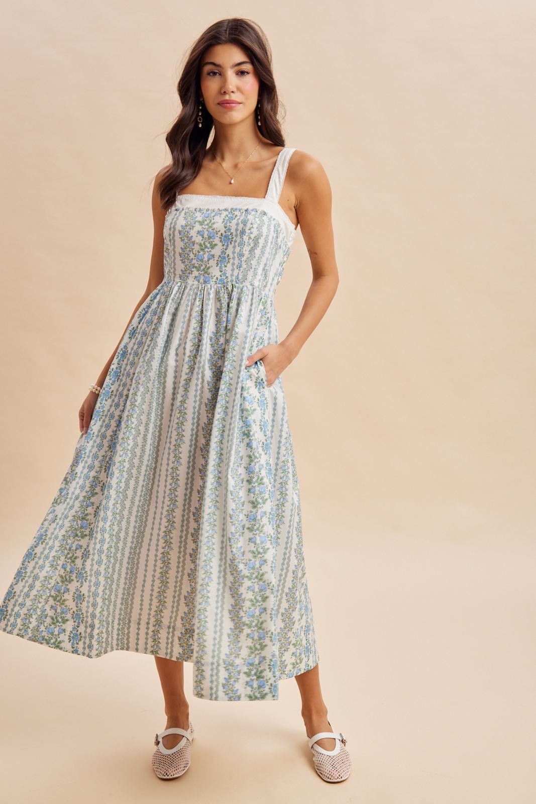 woman wearing a floral printed maxi dress with a fitted bodice, square neckline, and pockets, posed against a neutral background