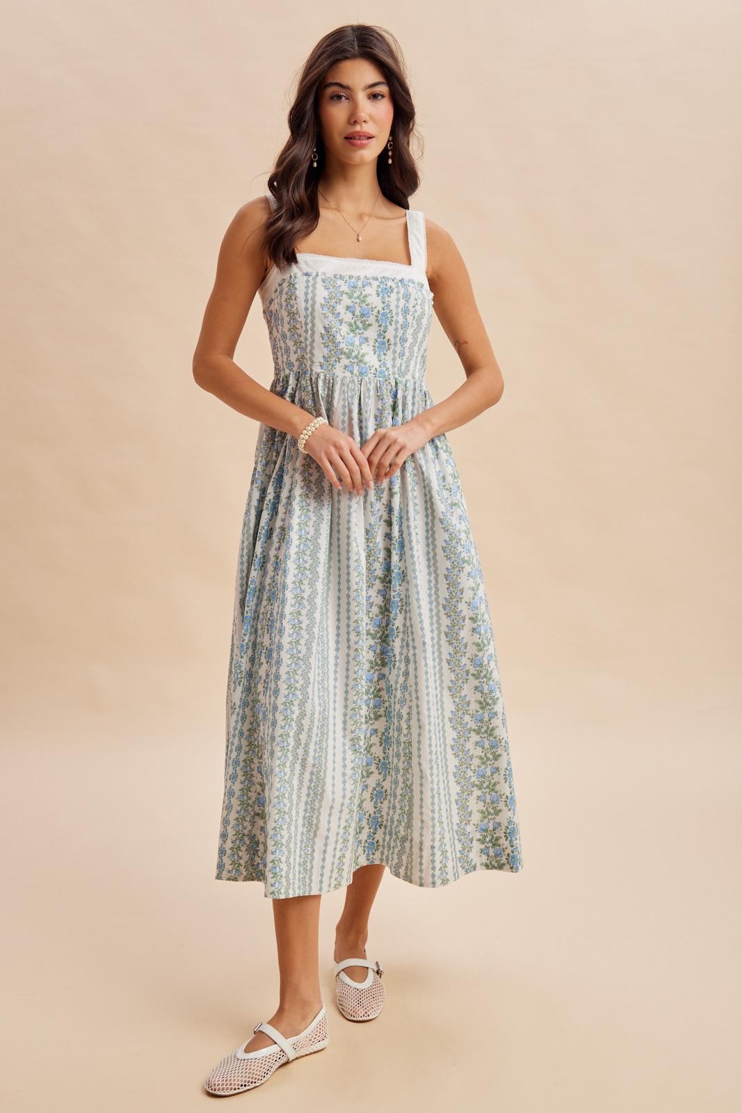 woman wearing a floral midi dress with a square neckline and wide straps, standing against a neutral background