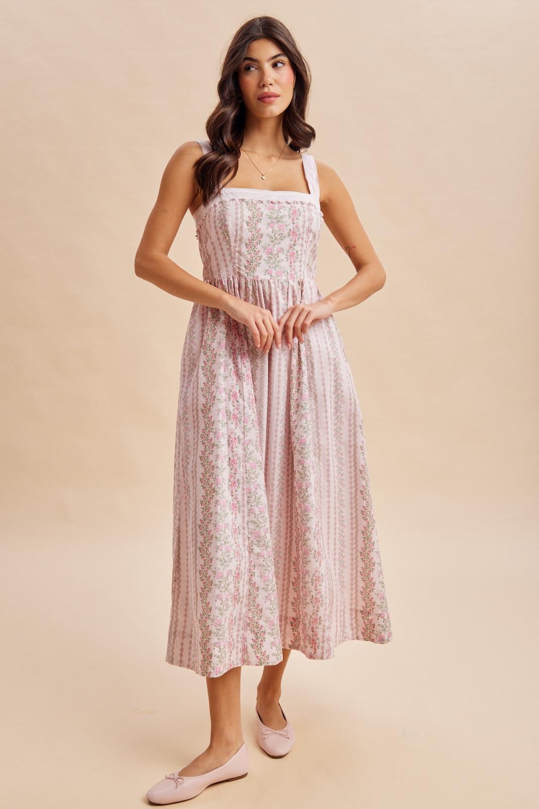 woman wearing a pink floral midi dress with square neckline and shoulder straps, standing on a beige background
