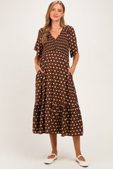 woman wearing a brown polka dot maternity dress with short sleeves and a tiered skirt, holding her baby bump