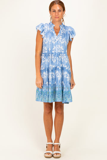 woman wearing a light blue floral print tiered dress with ruffle sleeves and a flared hem, standing against a plain background