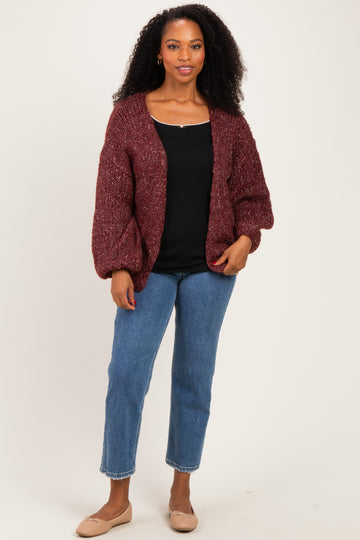 woman wearing a burgundy chunky knit cardigan over a black top, paired with light blue straight leg jeans and beige flats