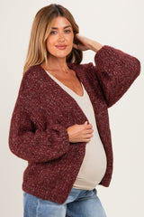 woman wearing a burgundy chunky knit maternity cardigan over a cream top and showing her baby bump