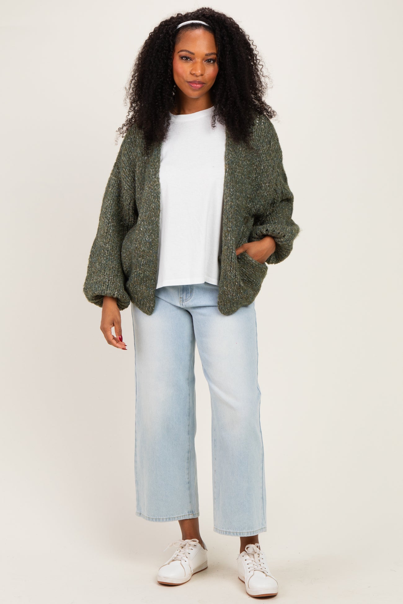 woman wearing a green chunky knit cardigan over a white t-shirt and light blue wide-leg jeans, styled with white sneakers