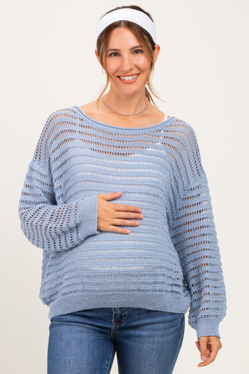 woman wearing a light blue maternity sweater with open knit design, smiling and holding her baby bump