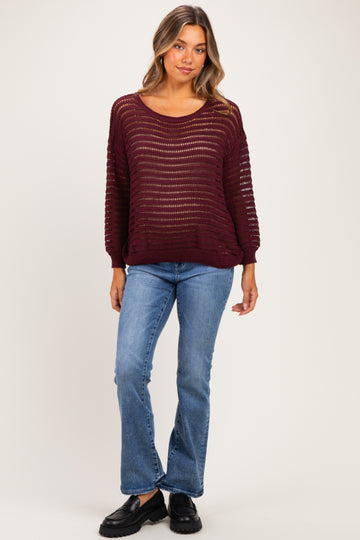 woman wearing a burgundy open knit maternity sweater with long sleeves and blue flared jeans