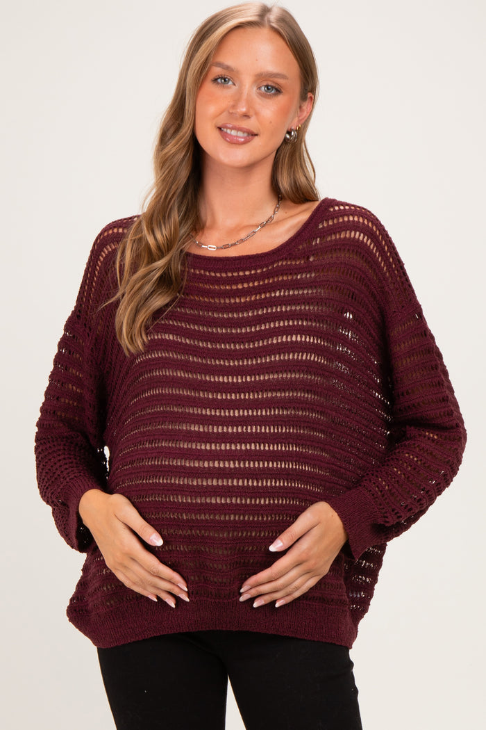 woman wearing a burgundy open knit maternity sweater and holding her baby bump