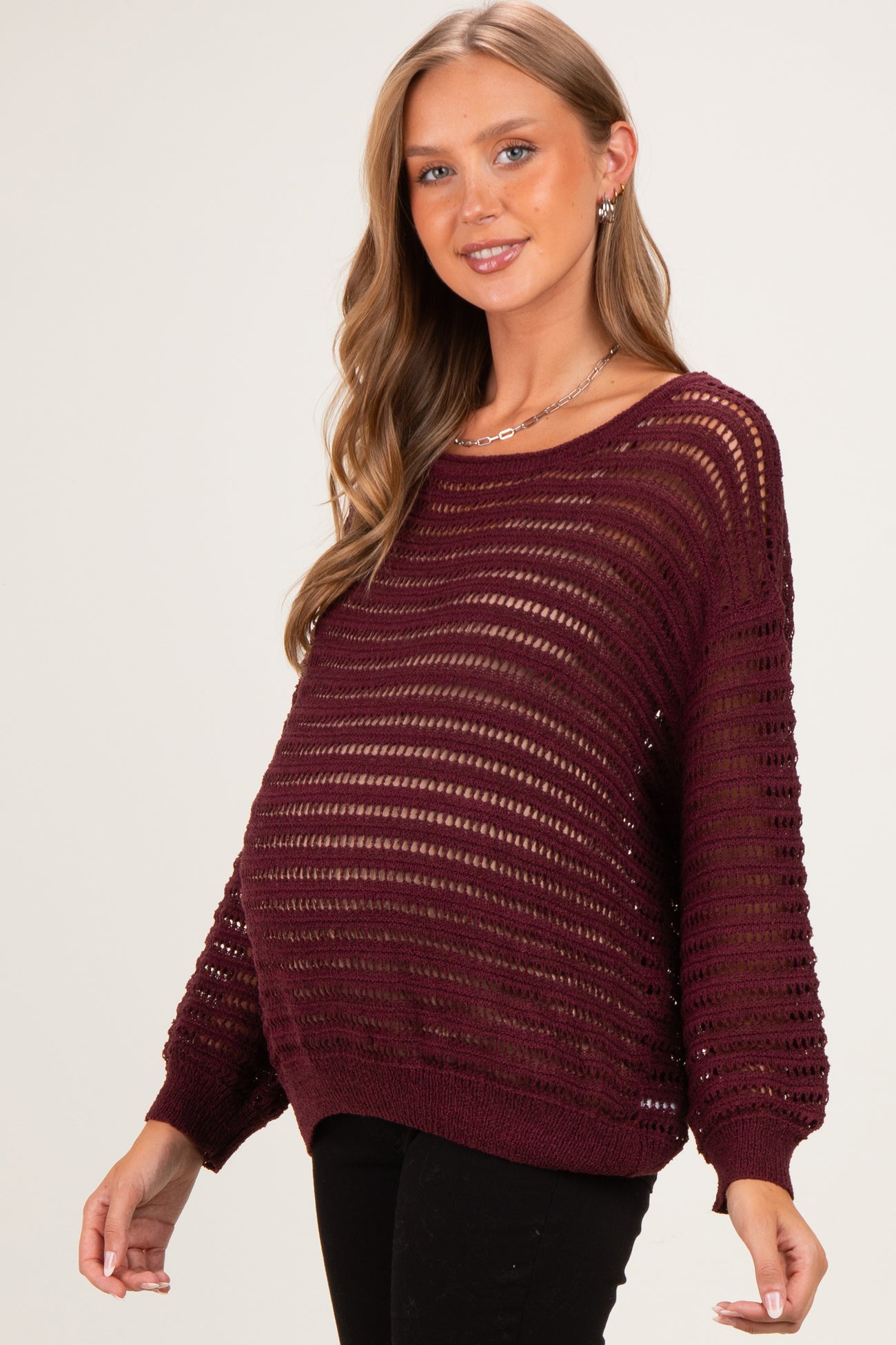 woman wearing a burgundy maternity sweater with open knit design and visible baby bump