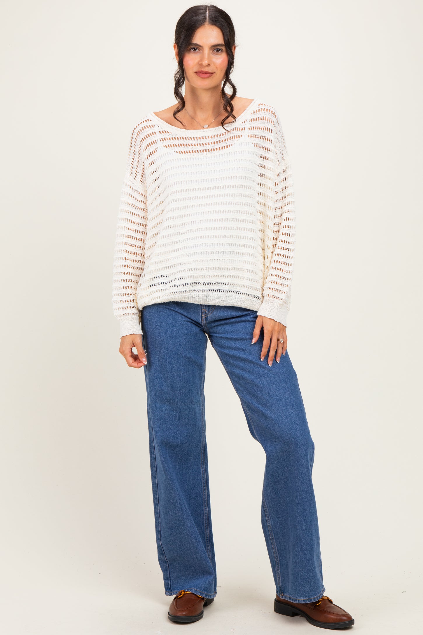 woman wearing a white open knit sweater and high-waisted blue jeans