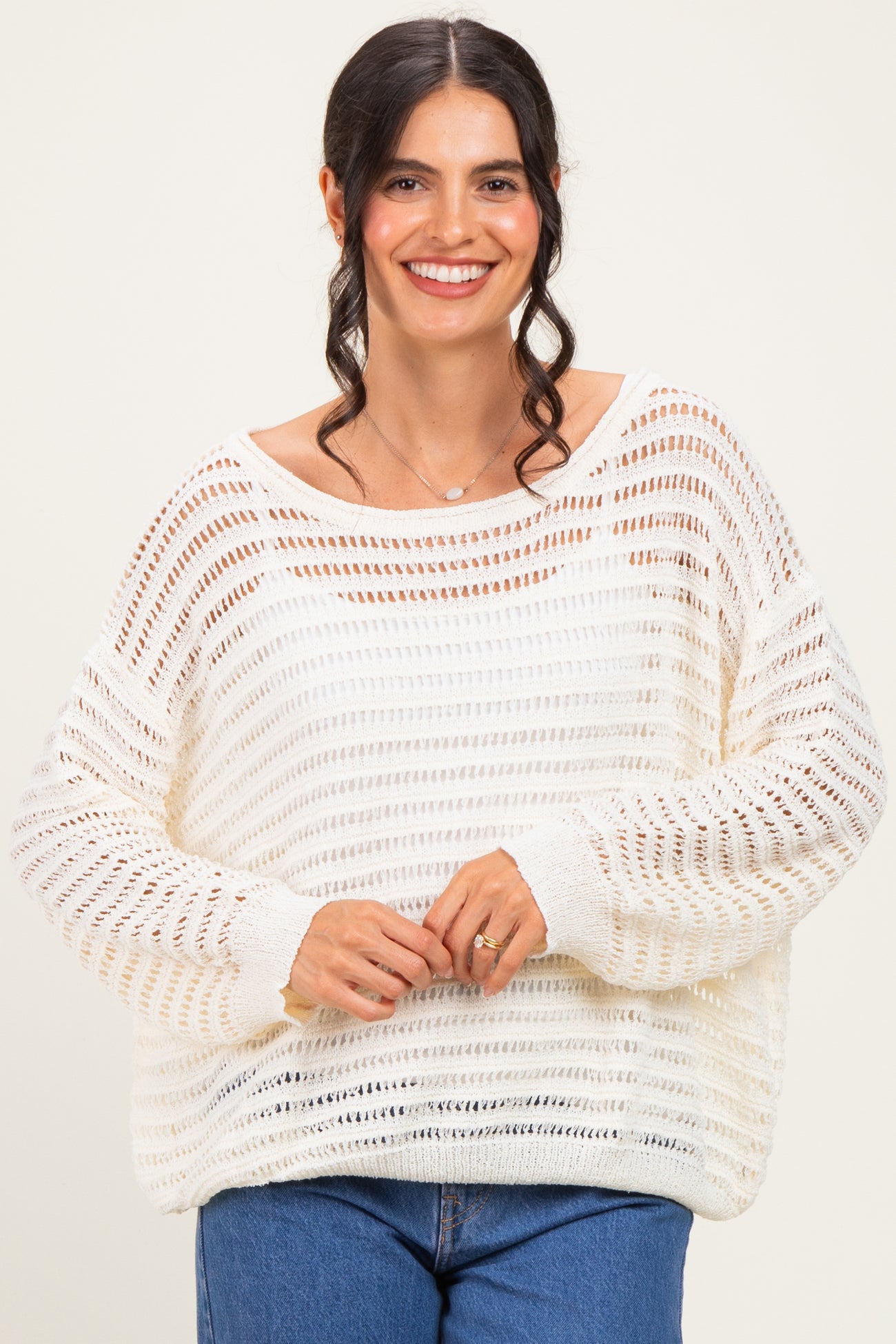 woman wearing a white open knit sweater with a relaxed fit and long sleeves, smiling at the camera