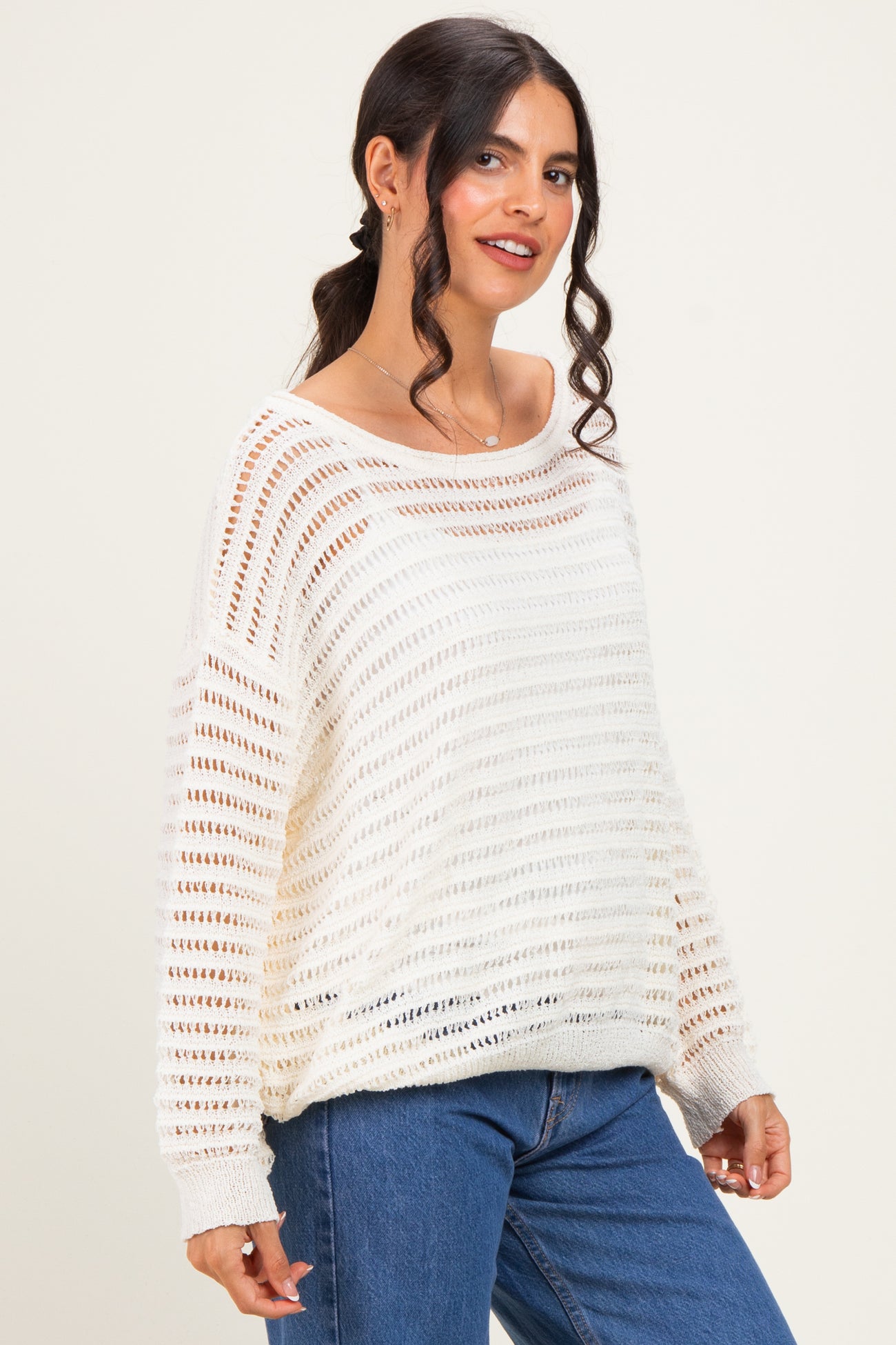 woman wearing a cream open knit oversized sweater with horizontal stripes and blue jeans
