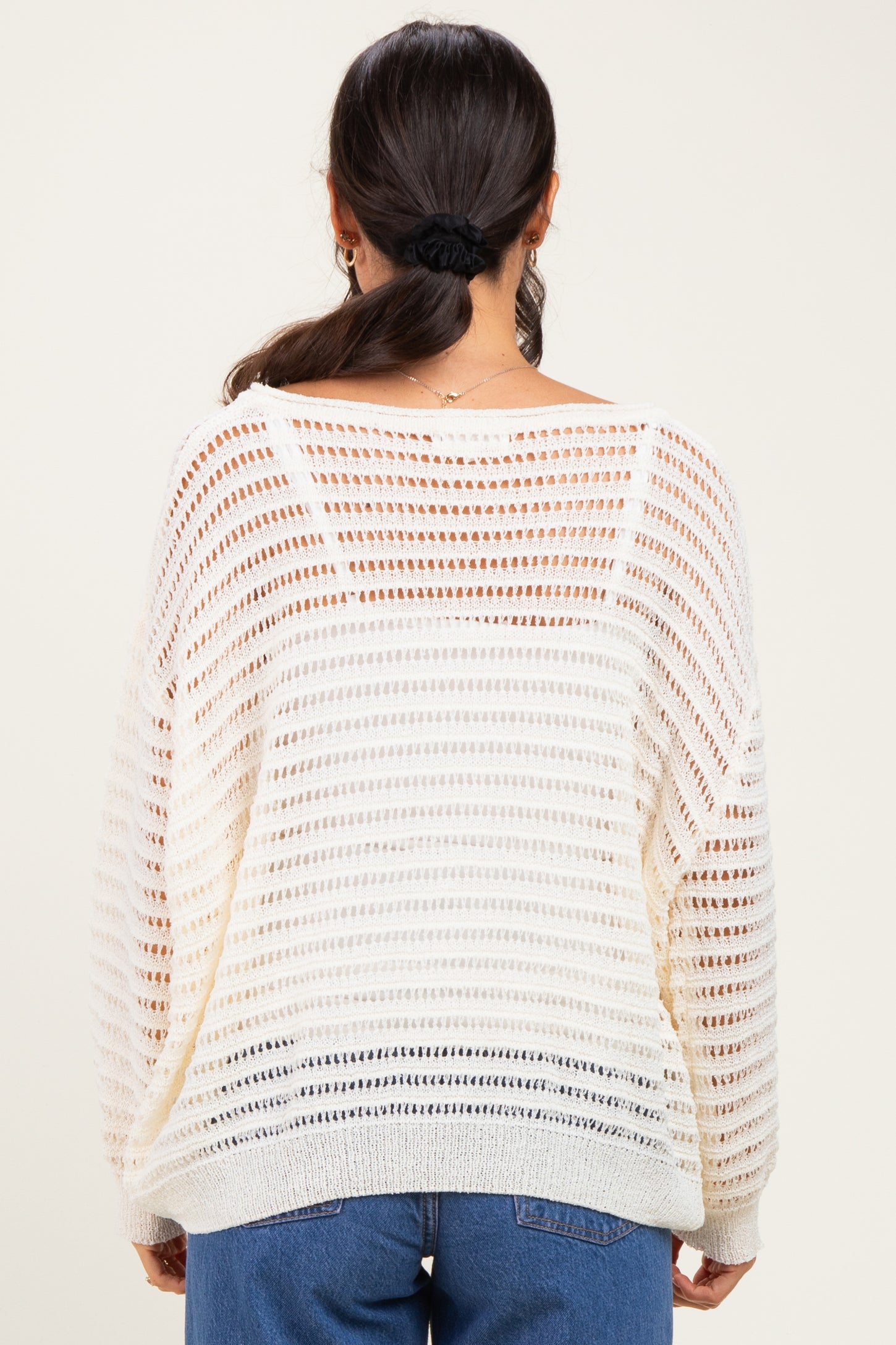 woman wearing a cream open-knit sweater with a loose fit and striped pattern, seen from the back