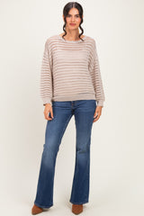 woman wearing a light brown open knit sweater and blue flared jeans, standing with a neutral background