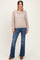 woman wearing a light brown open knit sweater and blue flared jeans, standing with a neutral background