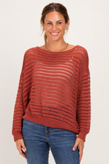 woman wearing a rust open-knit sweater with a relaxed fit and long sleeves, paired with blue jeans