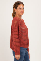 woman wearing a rust-colored open knit sweater with a relaxed fit and long sleeves, paired with blue jeans