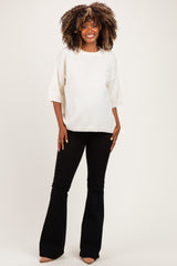 woman wearing a white short sleeve maternity sweater and black flared maternity pants, smiling and standing with hands on hips.