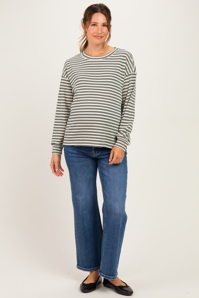 woman wearing a gray and white striped maternity top with long sleeves and blue wide-leg jeans, showing her baby bump
