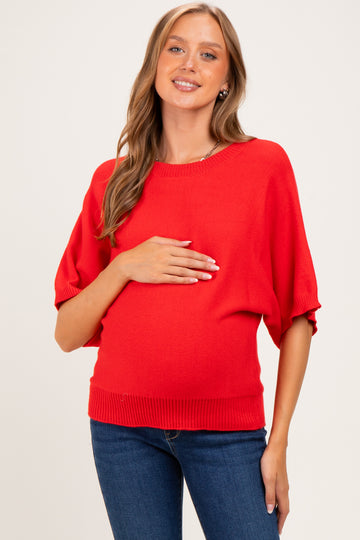 woman wearing a bright red maternity sweater with batwing sleeves and holding her baby bump