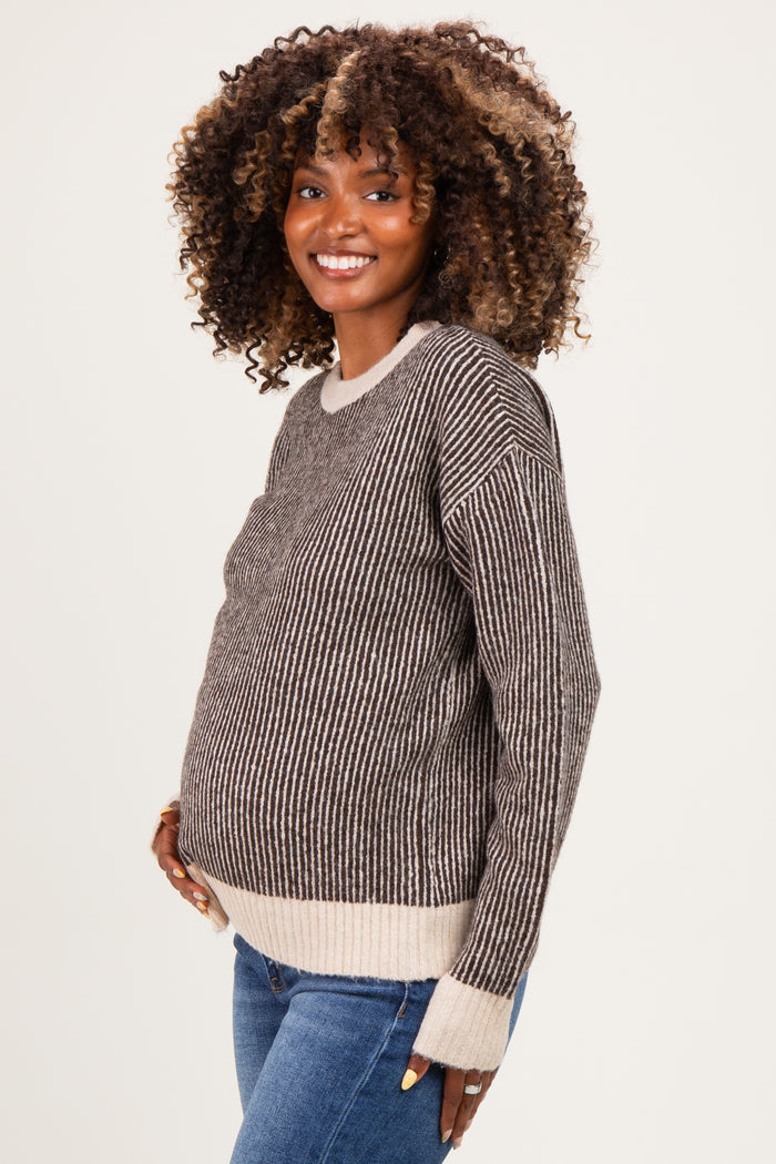 woman wearing a striped brown and cream maternity sweater and showcasing her baby bump