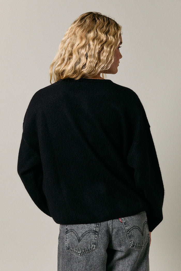 woman wearing a black oversized sweater with a relaxed fit, styled with gray jeans, viewed from the back