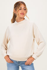 woman wearing a cream maternity sweatshirt with a high neck and balloon sleeves, showcasing her baby bump