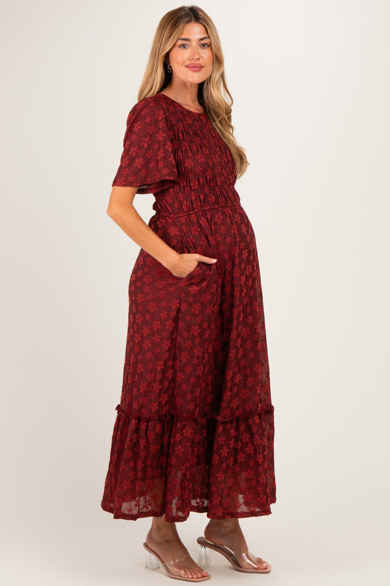 woman wearing a burgundy floral print maxi maternity dress with short sleeves and pockets, showcasing her baby bump