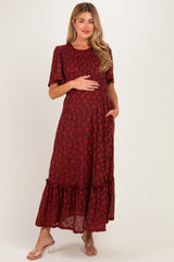 woman wearing a burgundy floral maternity dress with a ruffled hem and short sleeves, holding her baby bump