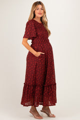woman wearing a burgundy floral print maxi maternity dress with short sleeves and pockets, showcasing her baby bump