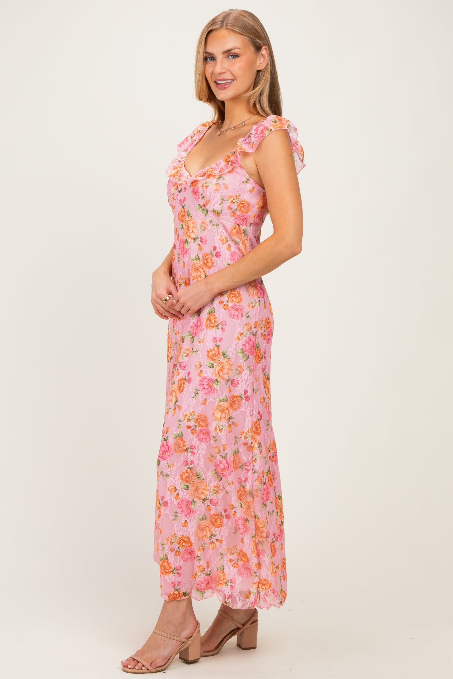 woman wearing a pink floral maxi dress with ruffled sleeves and a fitted bodice, standing elegantly