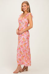 woman wearing a pink floral maxi dress with ruffled sleeves and a fitted bodice, standing elegantly