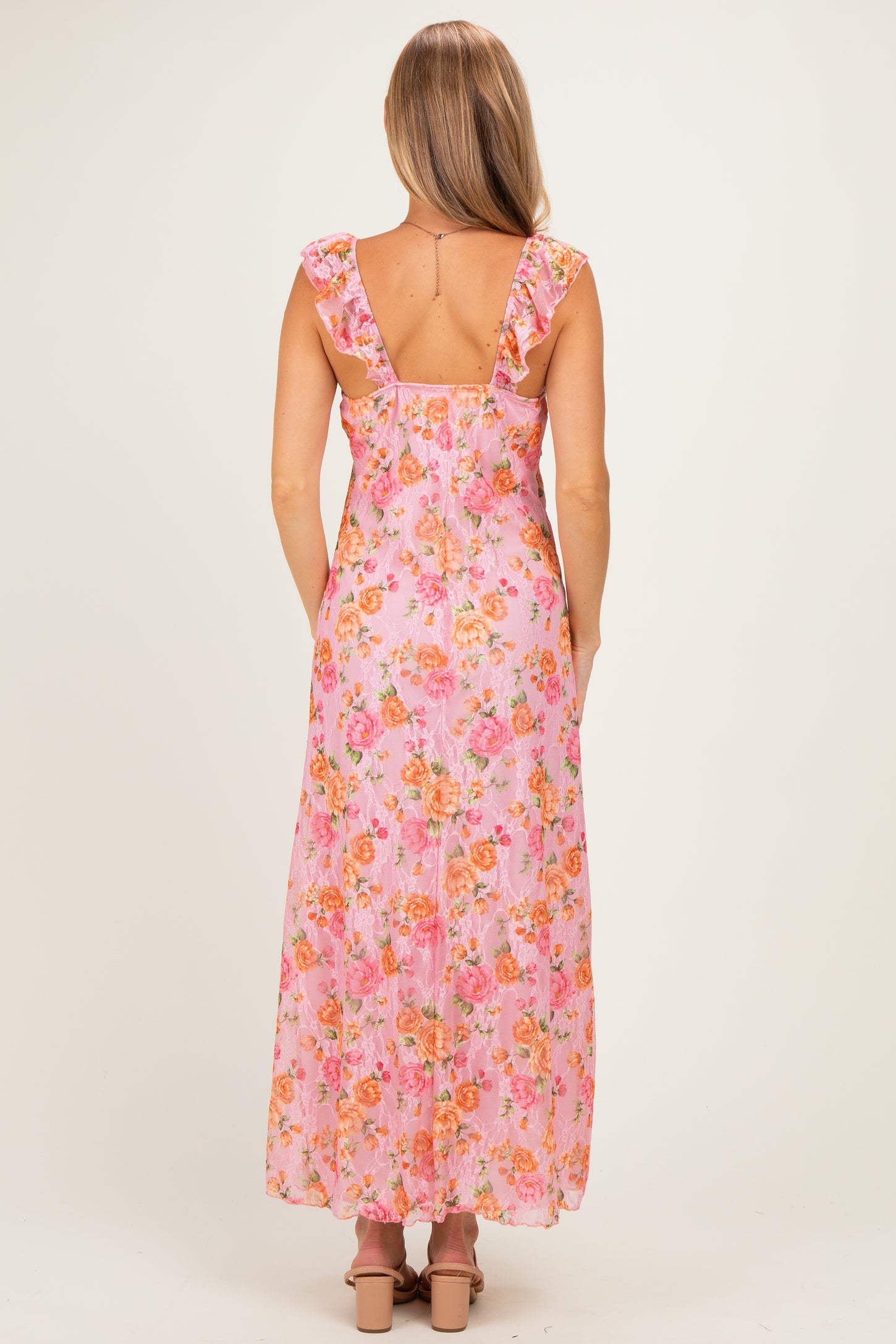 woman wearing a pink floral maxi dress with ruffled shoulder straps and an open back, seen from the back