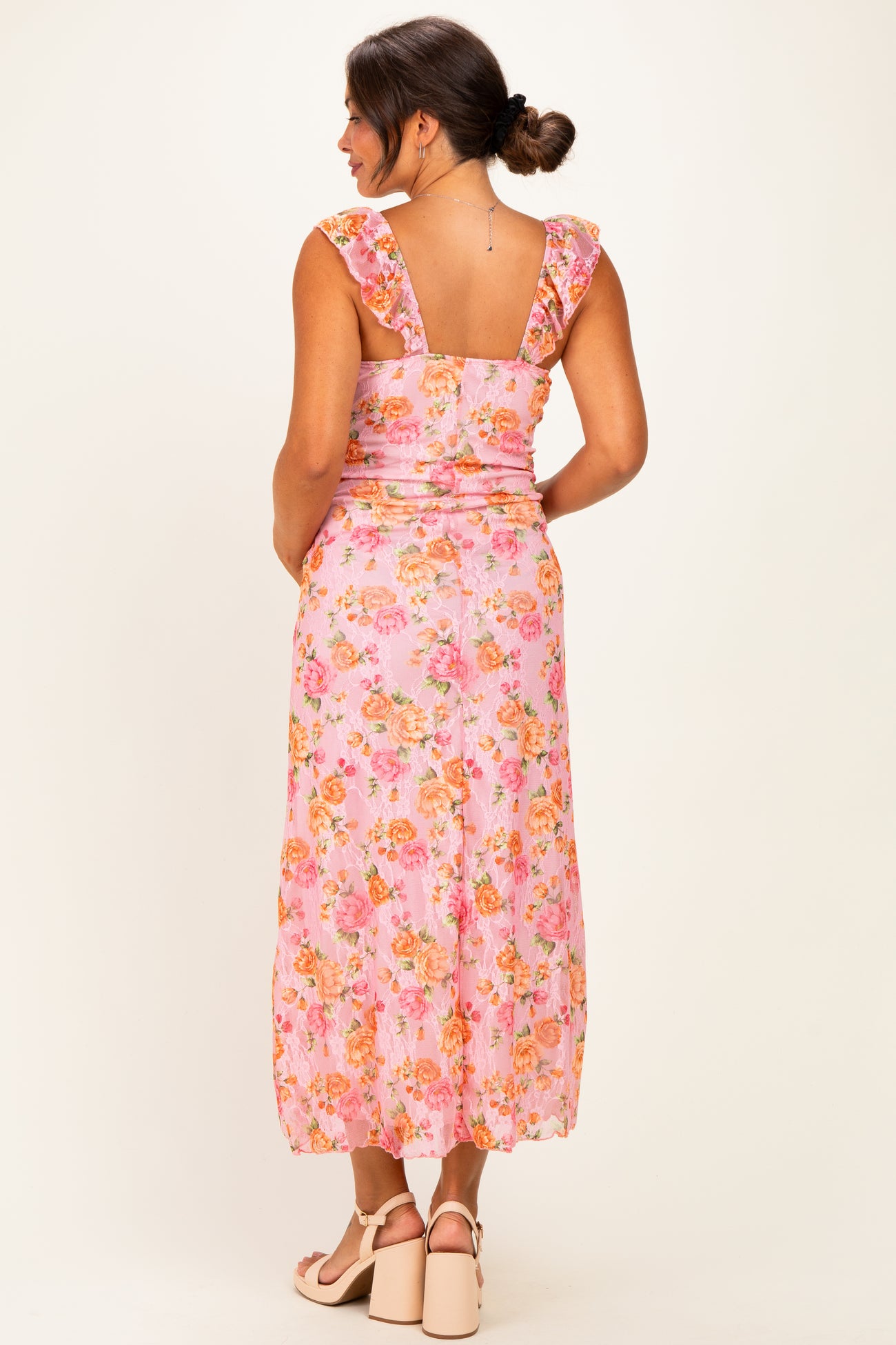 woman wearing a pink floral maternity dress with ruffled straps, showing a baby bump from the back