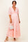 woman wearing a pink lace maternity dress with puff sleeves and ruffled hem, holding a white handbag and showing her baby bump