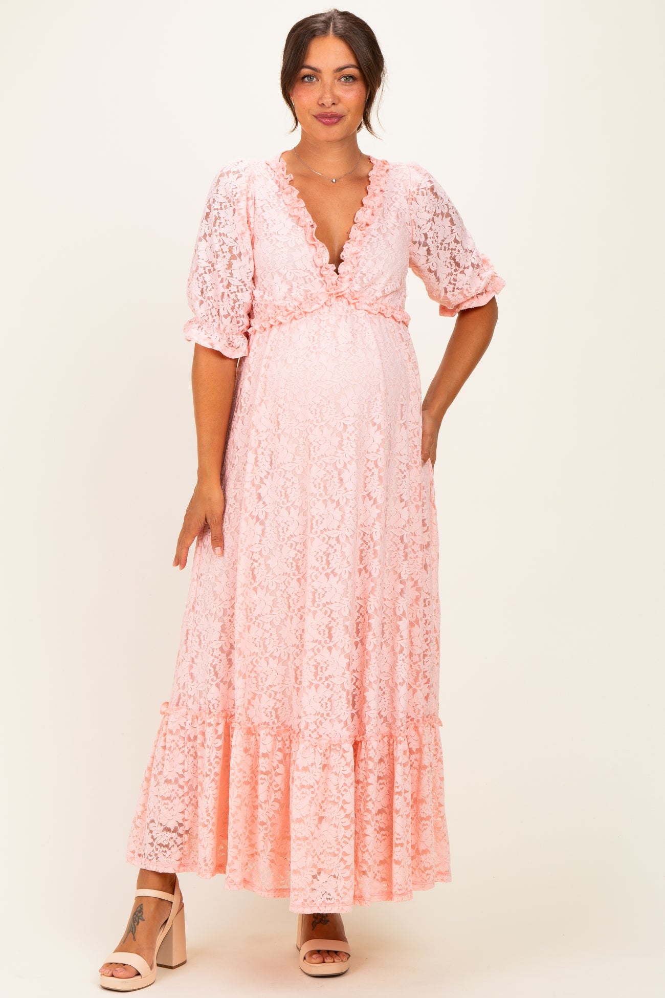 woman wearing a pink lace maternity maxi dress with a deep V-neck and ruffled sleeves, showcasing her baby bump