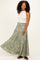 woman wearing a white sleeveless top and a flowing green patterned maxi skirt