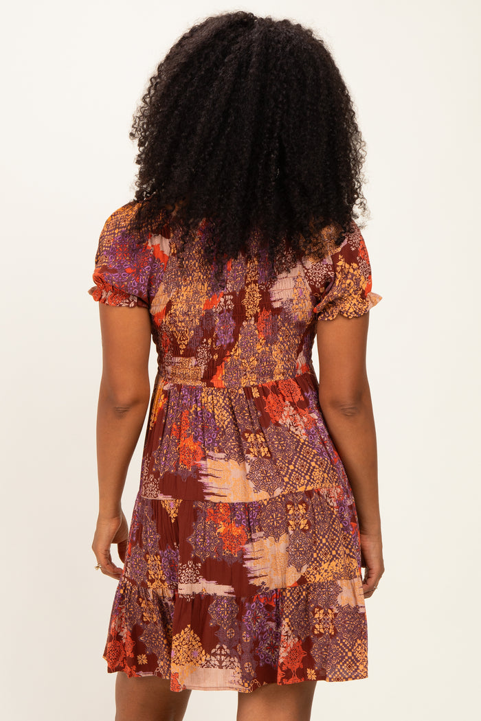 woman wearing a short-sleeve brown patterned dress with a flared skirt and a fitted bodice, seen from the back