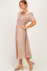 woman wearing a taupe polka dot midi dress with puff sleeves and smocked bodice, posed against a neutral background
