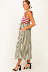 woman wearing a red and white striped sundress with a green and white striped skirt and pockets, standing in profile