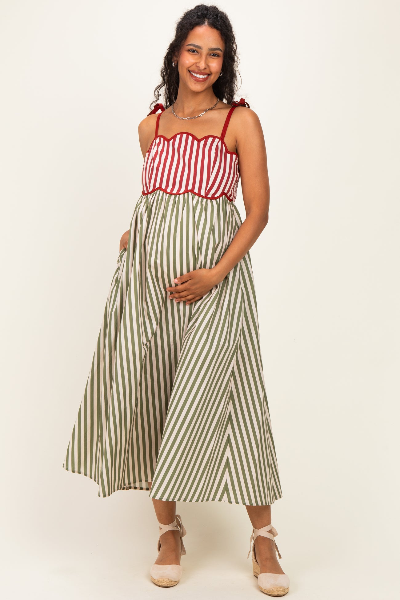 woman wearing a red and white striped maternity dress with a green striped bottom and holding her baby bump