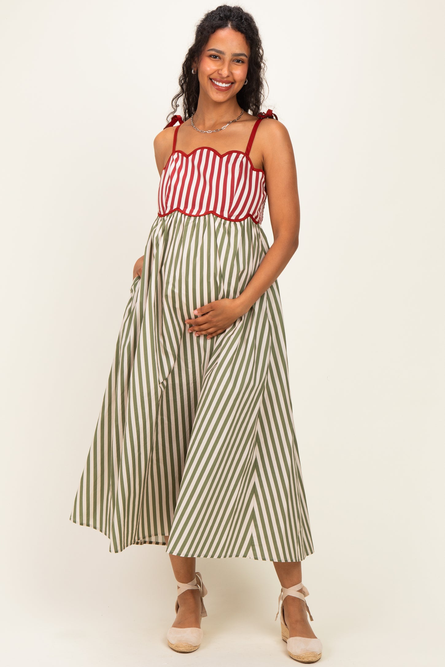 woman wearing a red and white striped maternity dress with a green striped bottom and holding her baby bump