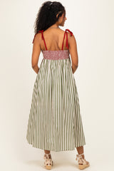 woman wearing a green and white striped maternity dress with red tie straps and a smocked bodice, showing a baby bump from the back