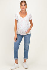 woman wearing a white short sleeve maternity top with floral prints and a visible baby bump, paired with rolled-up jeans