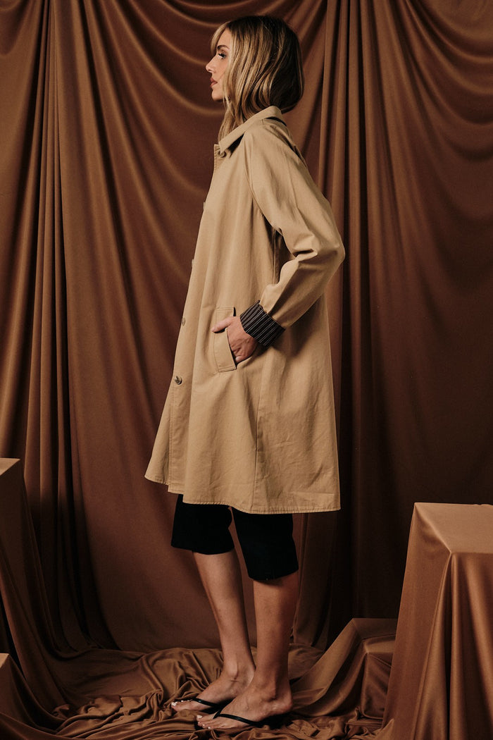 woman wearing a beige long coat with side pockets and a relaxed fit, styled with black shorts and flip flops