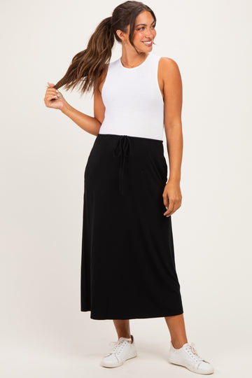 woman wearing a white sleeveless top and a black maternity maxi skirt with a drawstring detail and holding her hair