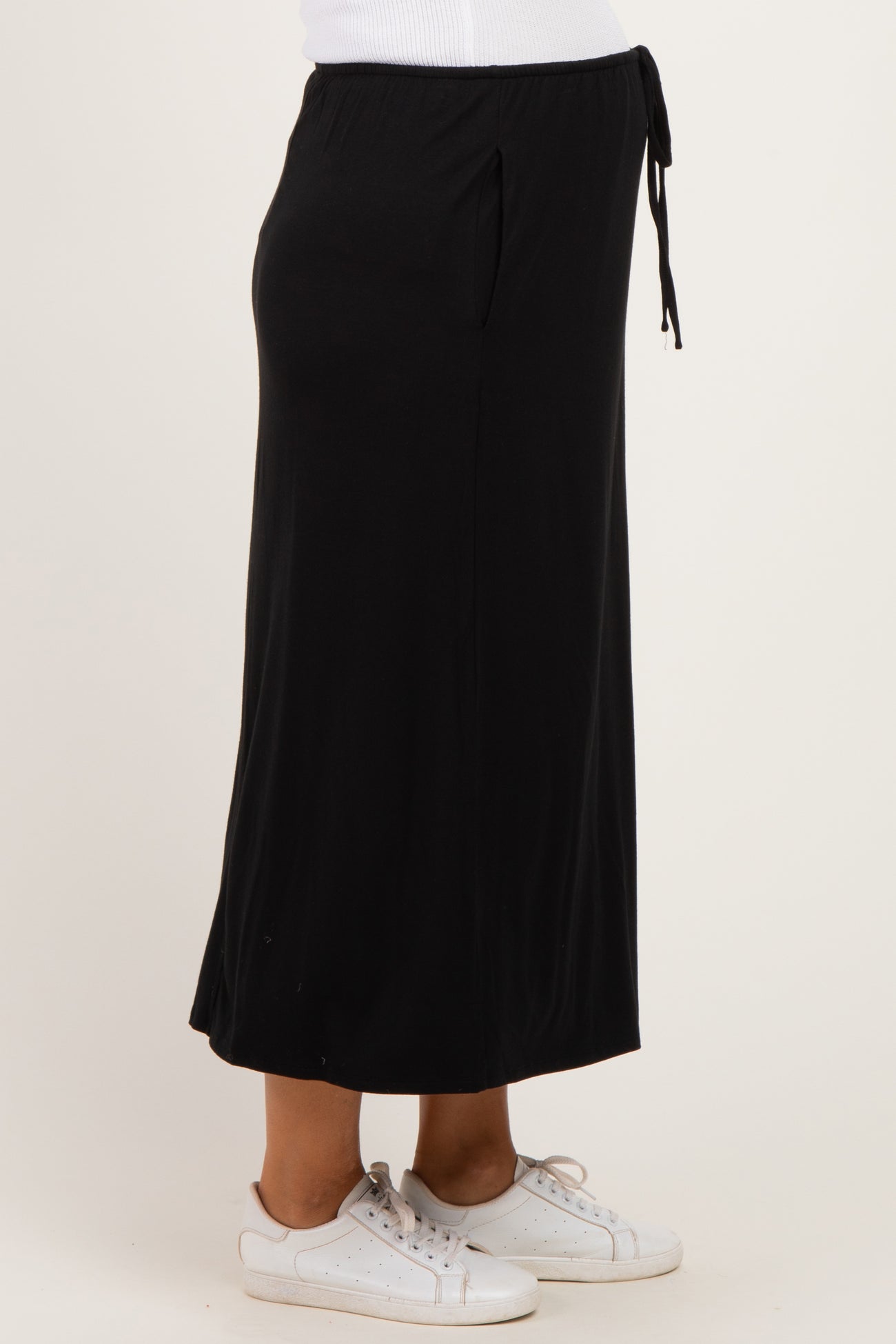 woman wearing a black maternity maxi skirt with adjustable tie and pockets, styled with white sneakers